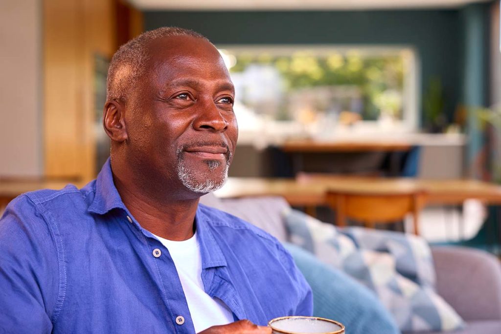 older man seated on couch at home drinking coffee while pondering why seek an independent living facility in beaumont, tx