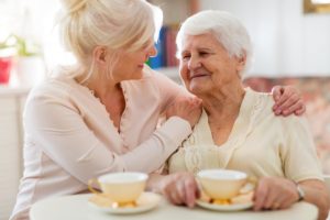 two older women sitting together at a table and drinking tea as one explains to the other what is respite care for seniors