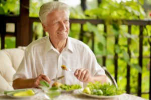 older gentleman sitting outside on deck smiling while eating heart healthy foods for seniors