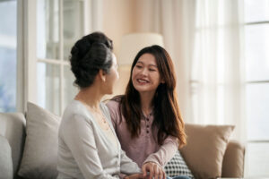 young woman seated on couch with her mother as she explores how to talk to senior parent about assisted living