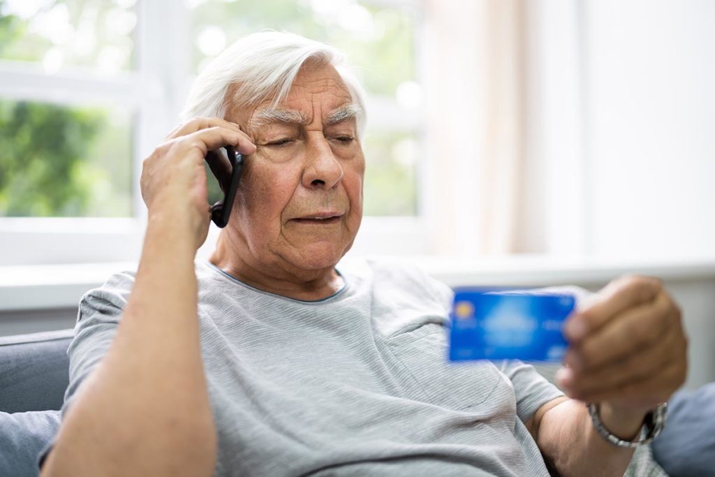 senior male on the phone with his credit card in his hand learning the hard way about the most common scams targeting seniors you need to know about