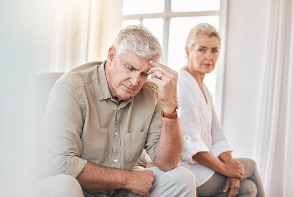 senior couple sitting on couch at home with wife looking at husband for sundowning symptoms and signs