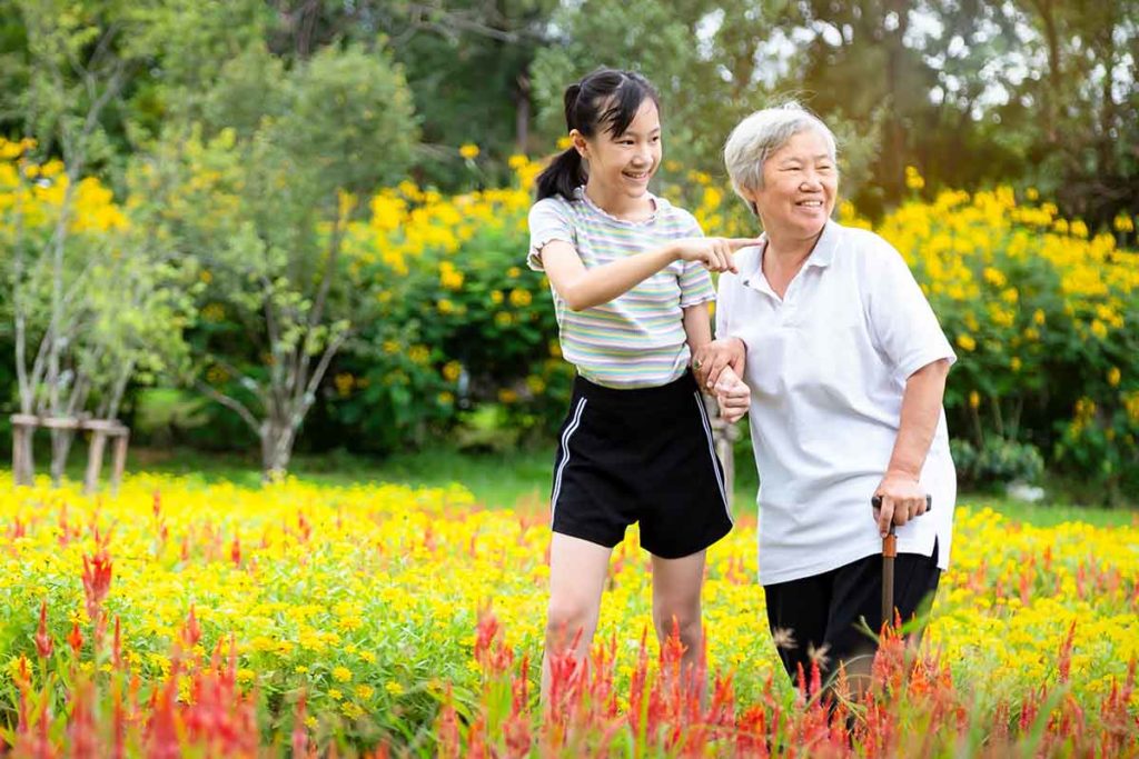 Woman walking her mother through a beautiful garden of flowers exploring the many benefits of sensory gardens for aging adults