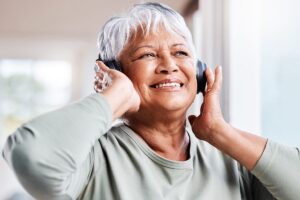 smiling older woman listening to music on headphones as part of sensory activities for dementia patients