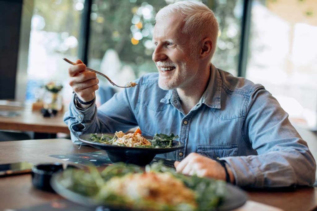 male senior citizen seated at table full of delicious food about to enjoy one of 5 health meals for seniors