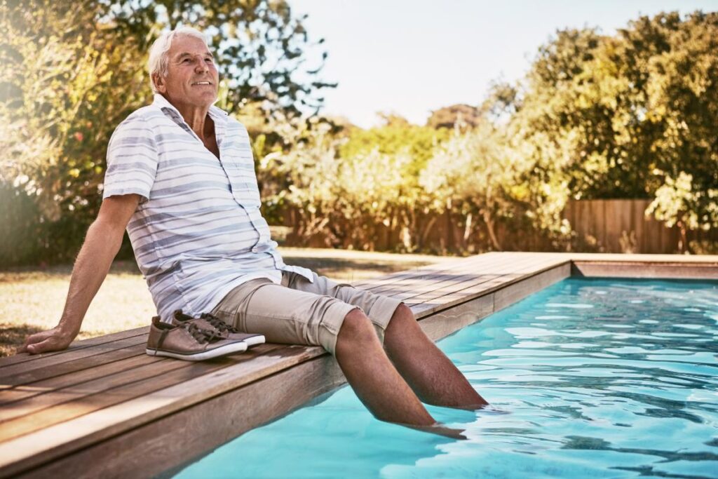 senior gentleman sitting on edge of pool with feet in the water enjoying one of 10 summer activities for senior citizens