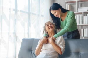 woman standing over her seated mother in the living room and affectionately reaching out wondering how can long term care services help my elderly parent