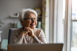 senior woman smiling as she researches on laptop independent living and how much does it cost
