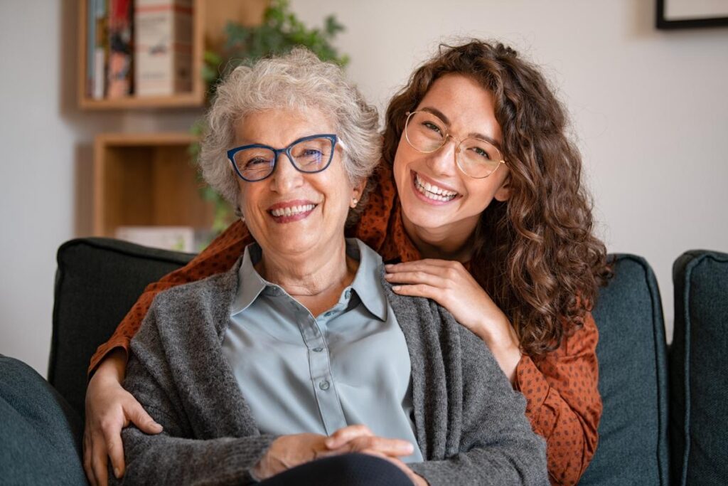younger woman hugging her aging mother as both smile and discuss assisted living and memory care services