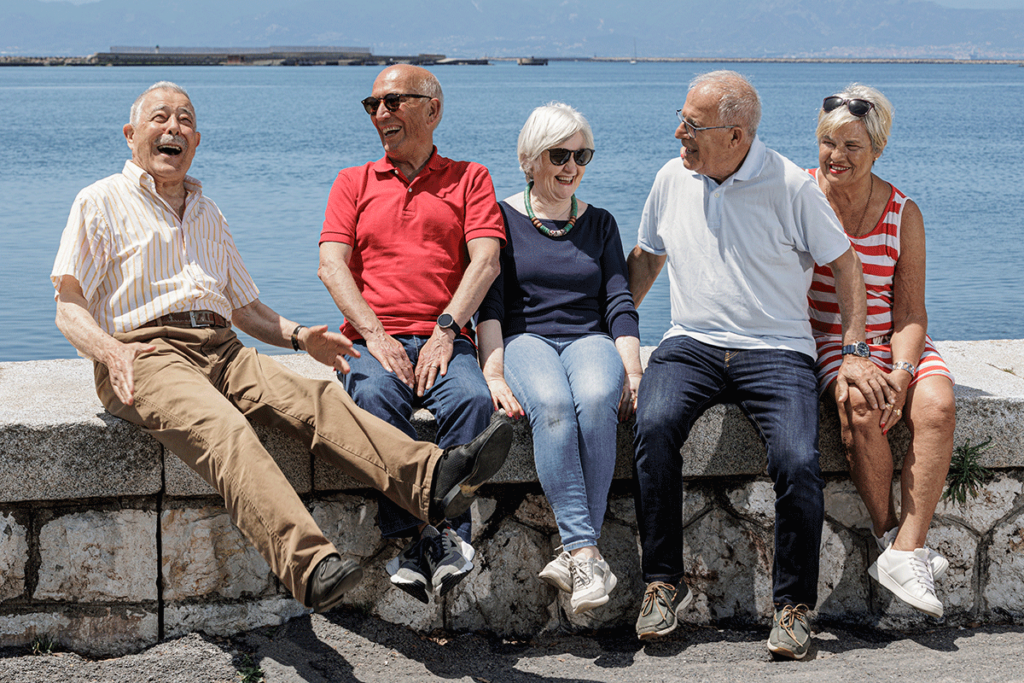 senior citizens seated outside on a wall overlooking water and smiling as they enjoy the benefits of community social events in senior independent living