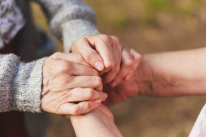 close up of younger hands clasping the hands of a senior adult as they discuss temporary vs. long-term respite care and which is right for your family