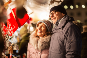 senior citizen couple dressed for winter standing outside enjoying safe and fun holiday decorations for senior living communities.